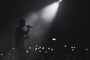 Silhueta de cantor com microfone sob spotlight em palco, plateia ao fundo com luzes