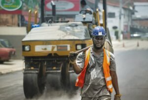 Trabalhador com colete refletivo e capacete em frente a maquina de pavimentacao em obra urbana