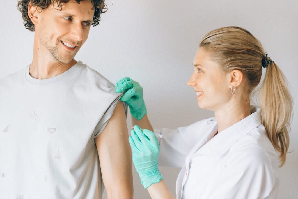 Profissional de saude com luva verde aplicando vacina no braco de paciente sorridente