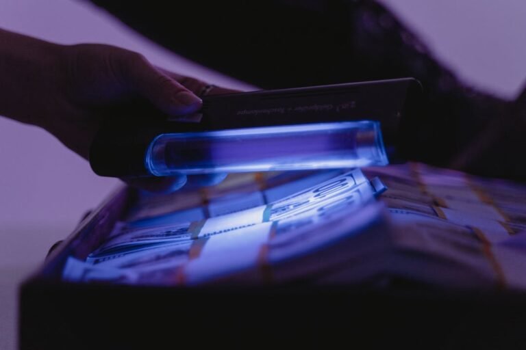 Cedulas de dinheiro sendo verificadas sob luz UV em equipamento de deteccao de falsificacao