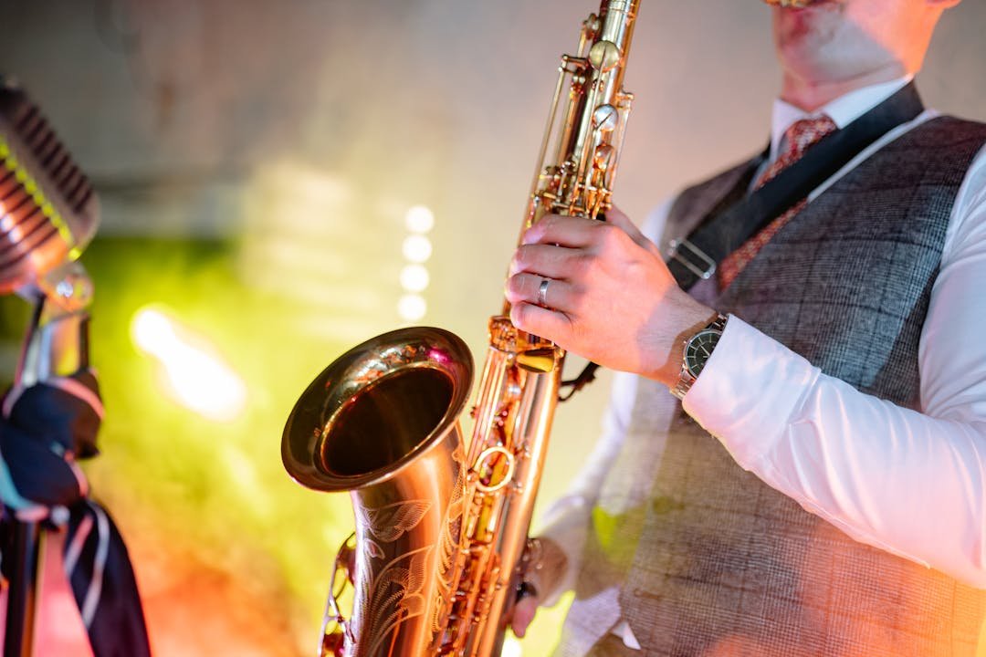 Saxofonista tocando saxofone tenor dourado em palco com microfone vintage