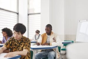 Estudantes diversos sentados em mesas de sala de aula fazendo prova com lapis