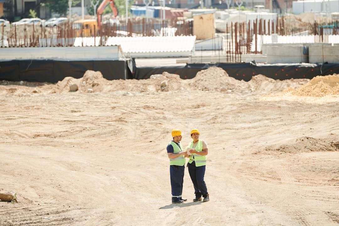 Trabalhadores com capacete e colete em terreno de obra civil em fase inicial