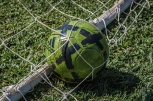 Bola de futebol verde dentro de rede de gol em campo gramado