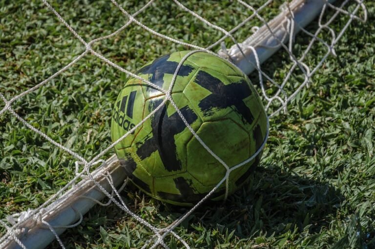 Bola de futebol verde dentro de rede de gol em campo gramado