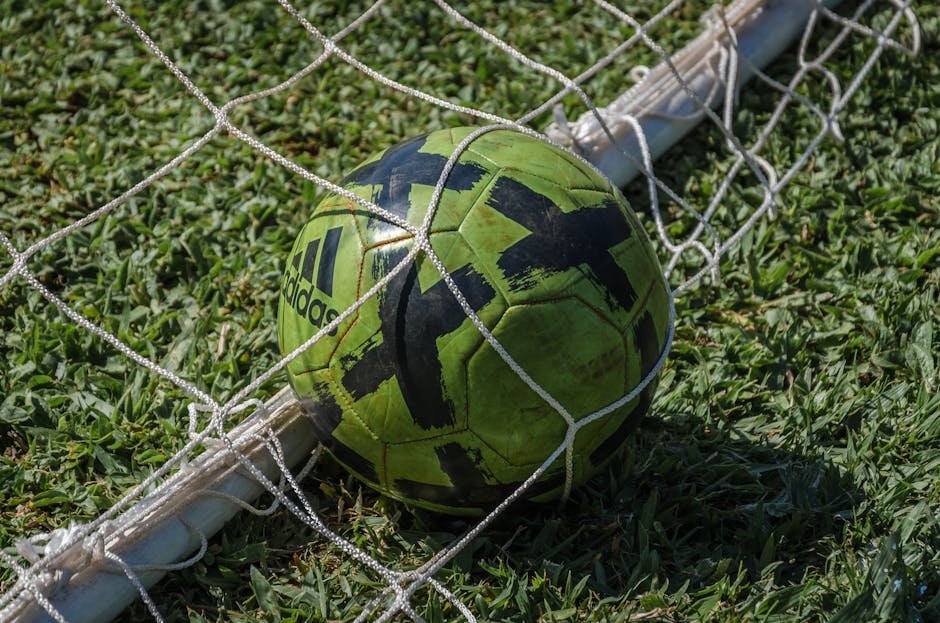 Bola de futebol verde dentro de rede de gol em campo gramado
