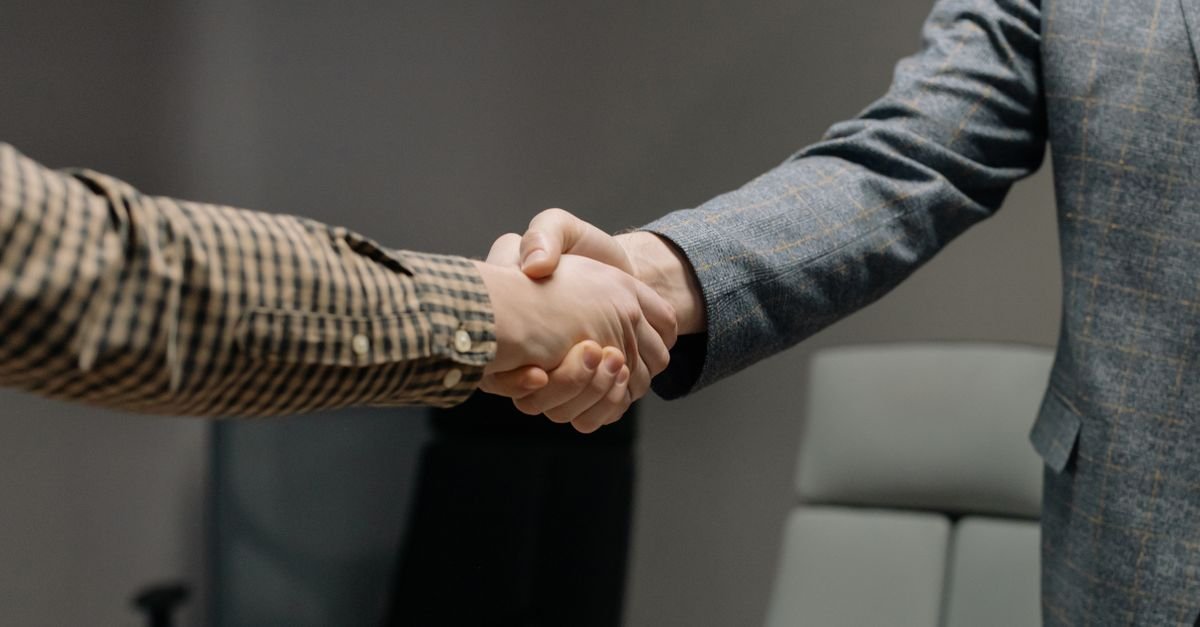 Aperto de mãos entre duas pessoas em escritório, simbolizando contratação de emprego