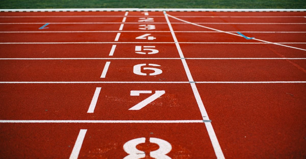 Pista de atletismo vermelha com raias numeradas de 1 a 8 na linha de largada