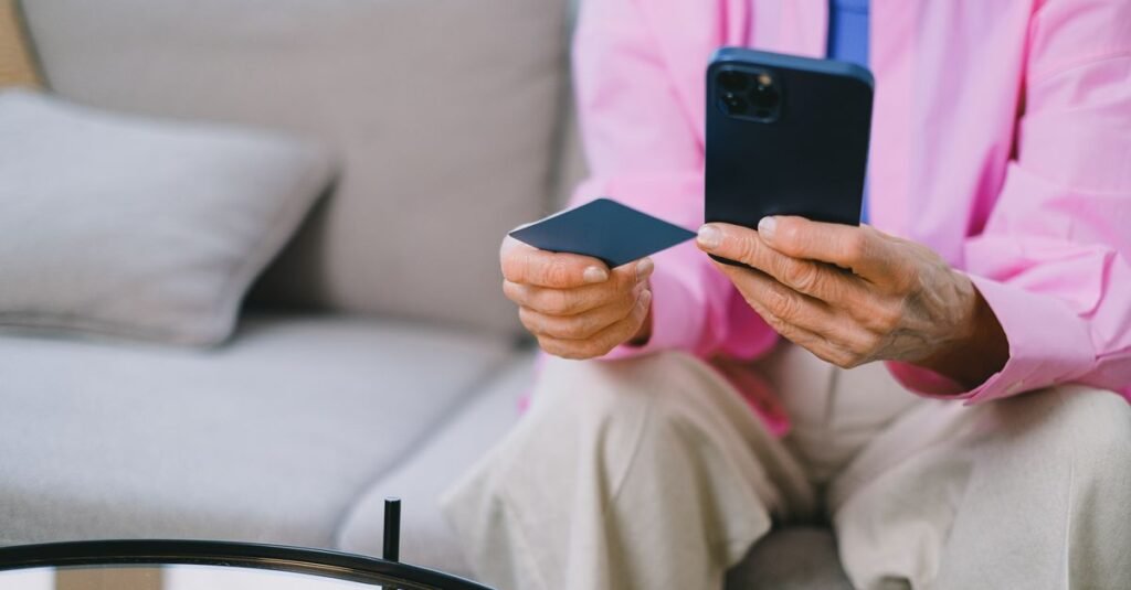 Pessoa idosa segura cartão e celular para consultar pagamento de benefício