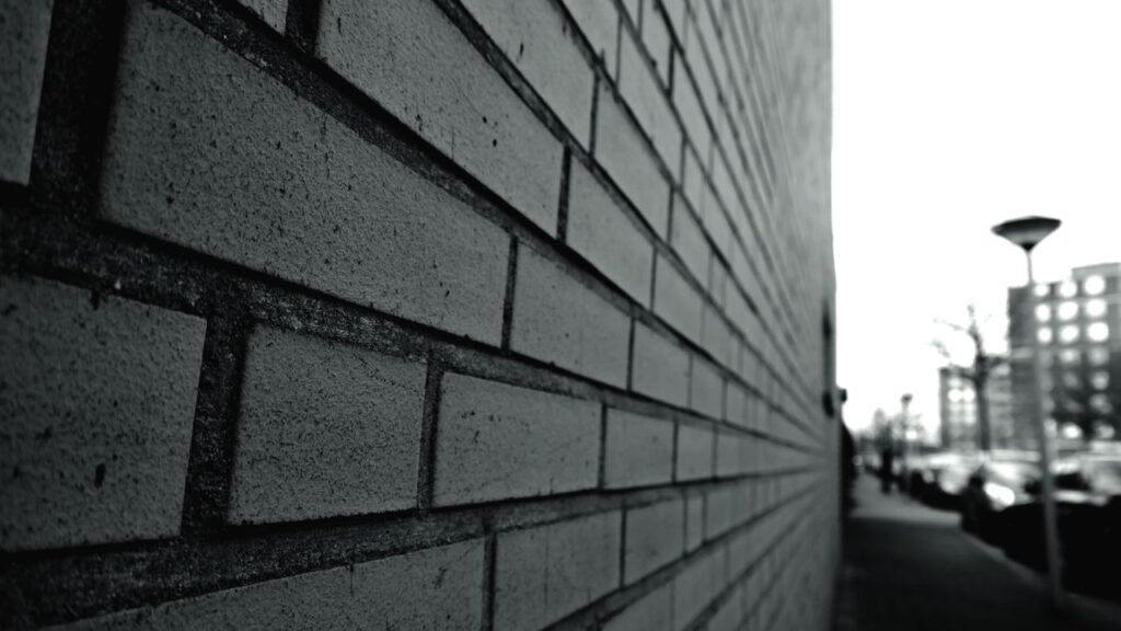 Muro de tijolos em preto e branco visto em perspectiva, com rua ao fundo