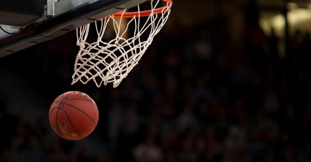 Bola de basquete entra na cesta durante jogo em ginásio