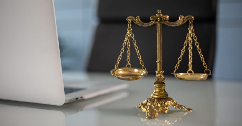 Balança da justiça dourada sobre mesa ao lado de laptop