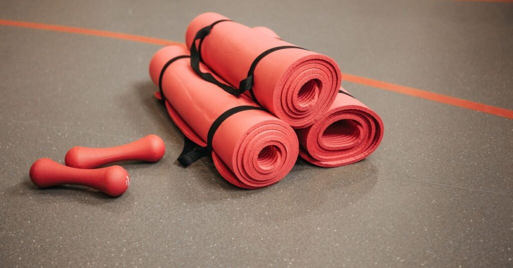 Tapetes de exercício enrolados e halteres vermelhos no piso de uma academia