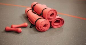 Tapetes de exercício enrolados e halteres vermelhos no piso de uma academia