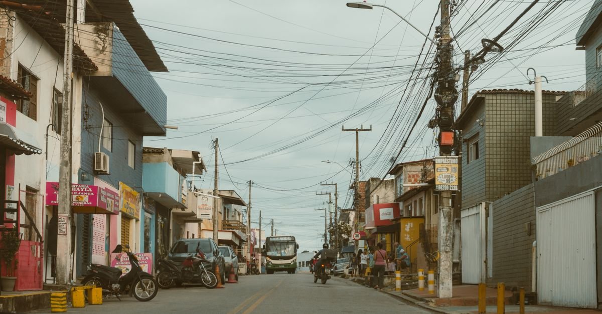 Rua comercial brasileira com lojas, motos e ônibus em dia nublado