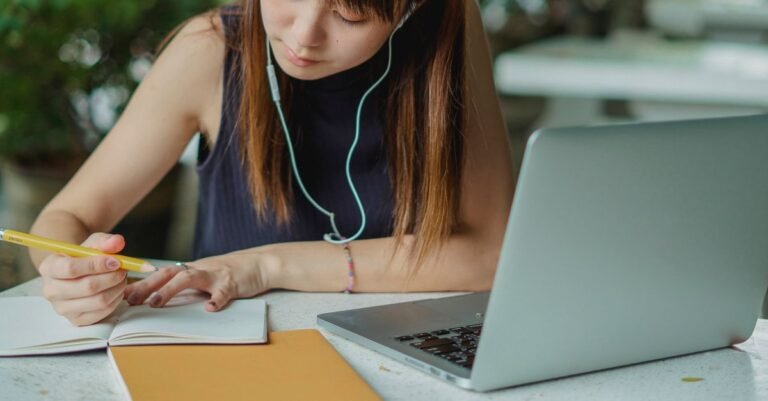 Estudante faz anotações em caderno ao lado de laptop durante preparação para prova