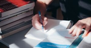 Pessoa estudando com caderno e livros empilhados, representando preparação para concurso