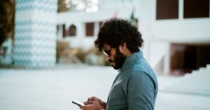 Homem de óculos usando um aplicativo no celular em área externa durante o dia