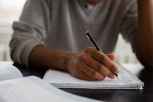 Estudante adulto escreve em caderno durante aula