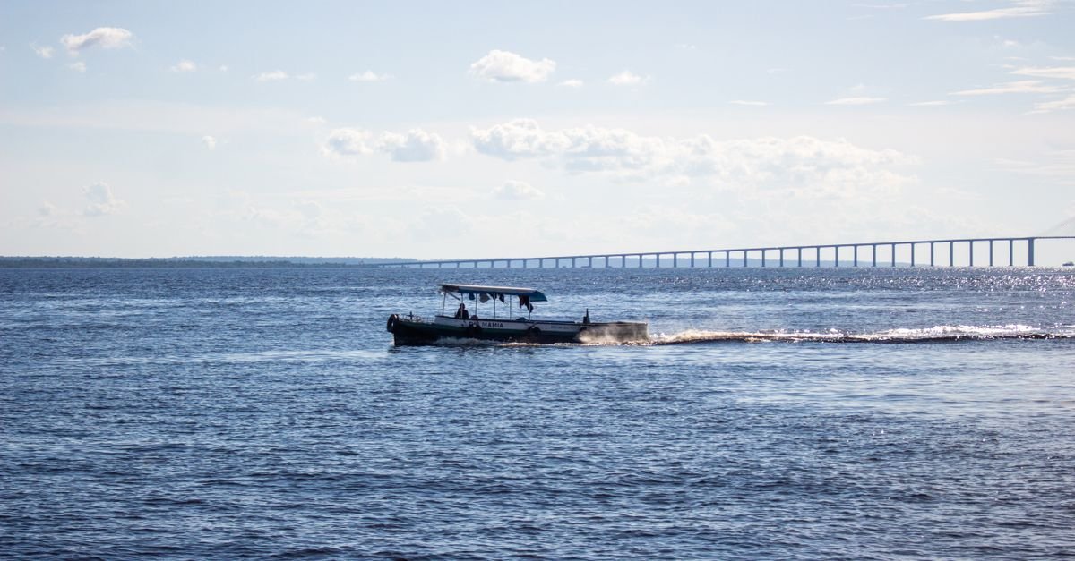 Barco regional de passageiros navega no Rio Negro com a ponte de Manaus ao fundo