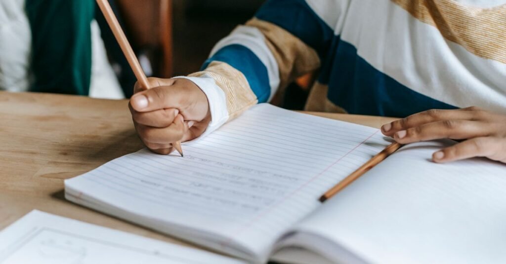 Crianca escreve a lapis em caderno sobre carteira escolar