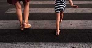 Mãe e criança atravessam a rua sobre faixa de pedestres