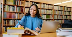 Estudante faz anotações em biblioteca com livros e notebook