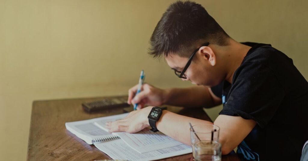 Estudante escreve em caderno sobre mesa de madeira durante estudo