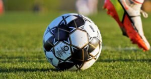 Bola de futebol em gramado com chuteira ao fundo