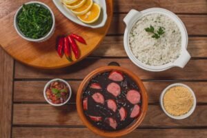 Prato de feijoada com arroz, couve e laranja em mesa de madeira
