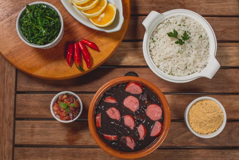 Prato de feijoada com arroz, couve e laranja em mesa de madeira