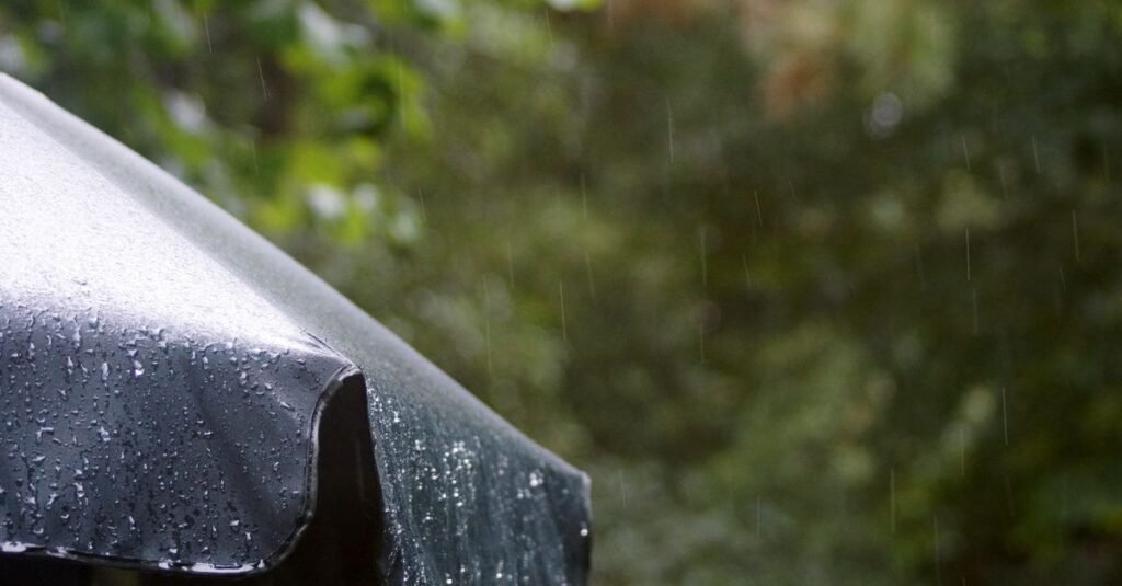 Guarda-chuva coberto de gotas durante chuva com vegetação ao fundo