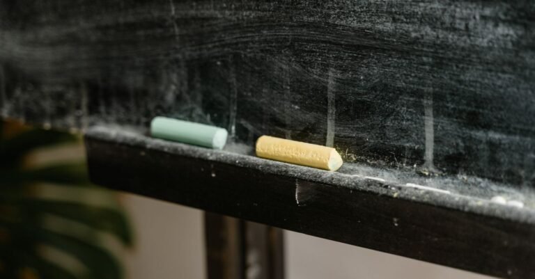 Dois gizes coloridos apoiados na borda de um quadro-negro de sala de aula