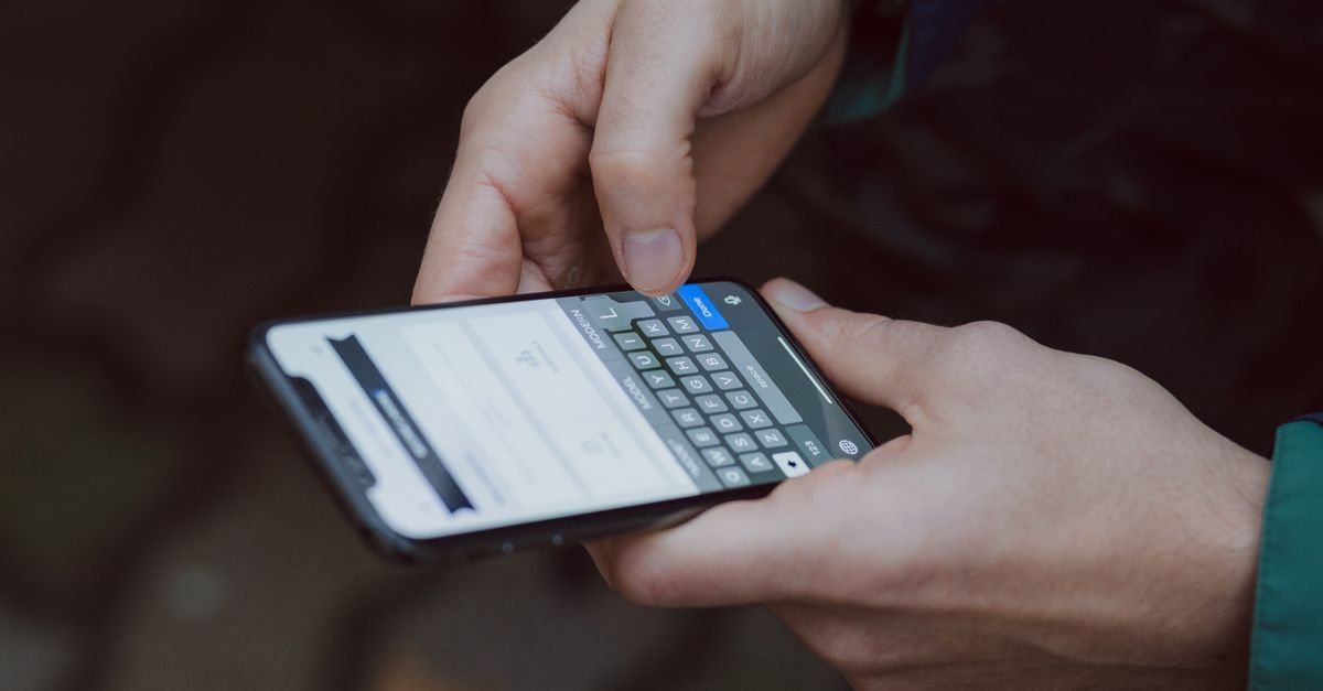Mãos de uma pessoa digitando mensagem na tela de um celular