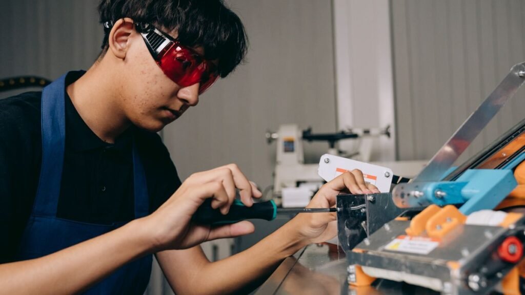 Jovem aprendiz com óculos de proteção opera máquina em oficina