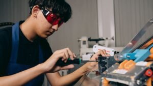 Jovem aprendiz com óculos de proteção opera máquina em oficina