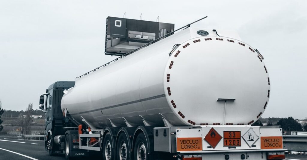 Caminhão-tanque de combustível visto de trás em rodovia, com placas de risco de produto inflamável