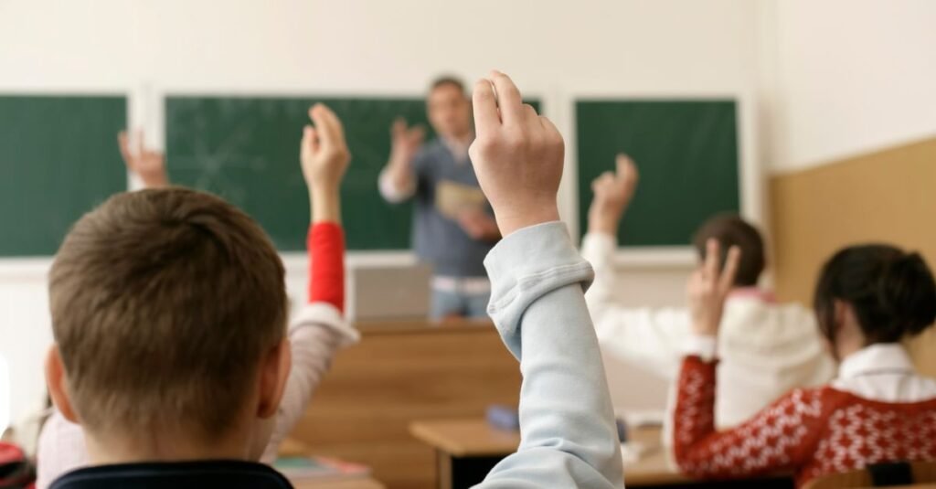 Alunos levantam a mão em sala de aula durante explicação do professor