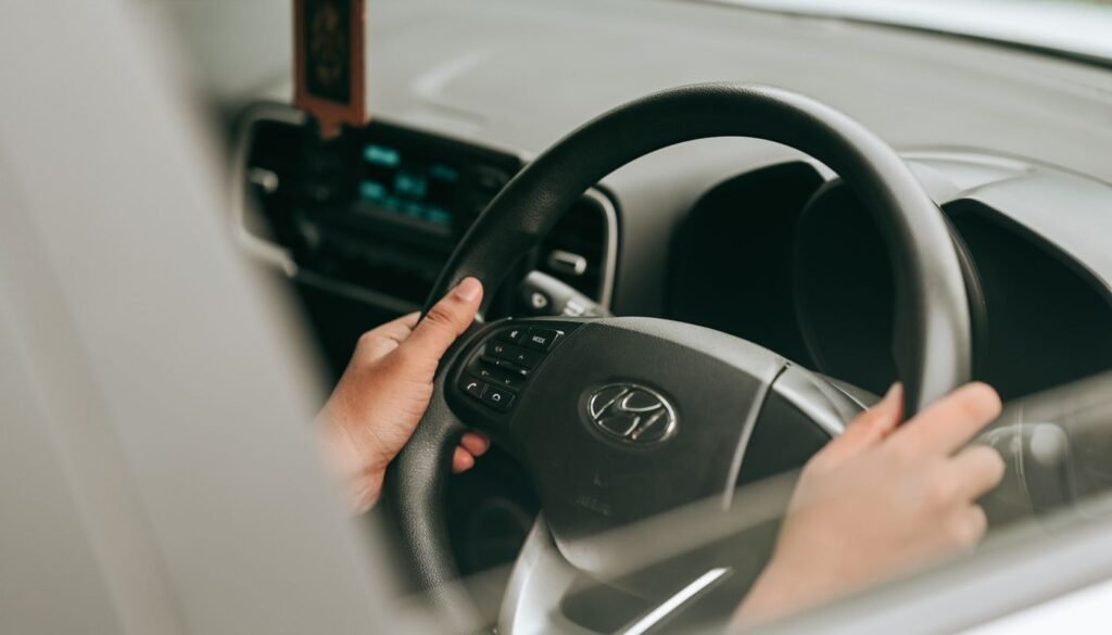 Mãos de motorista no volante de um carro, vistas pela janela do veículo