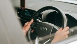 Mãos de motorista no volante de um carro, vistas pela janela do veículo