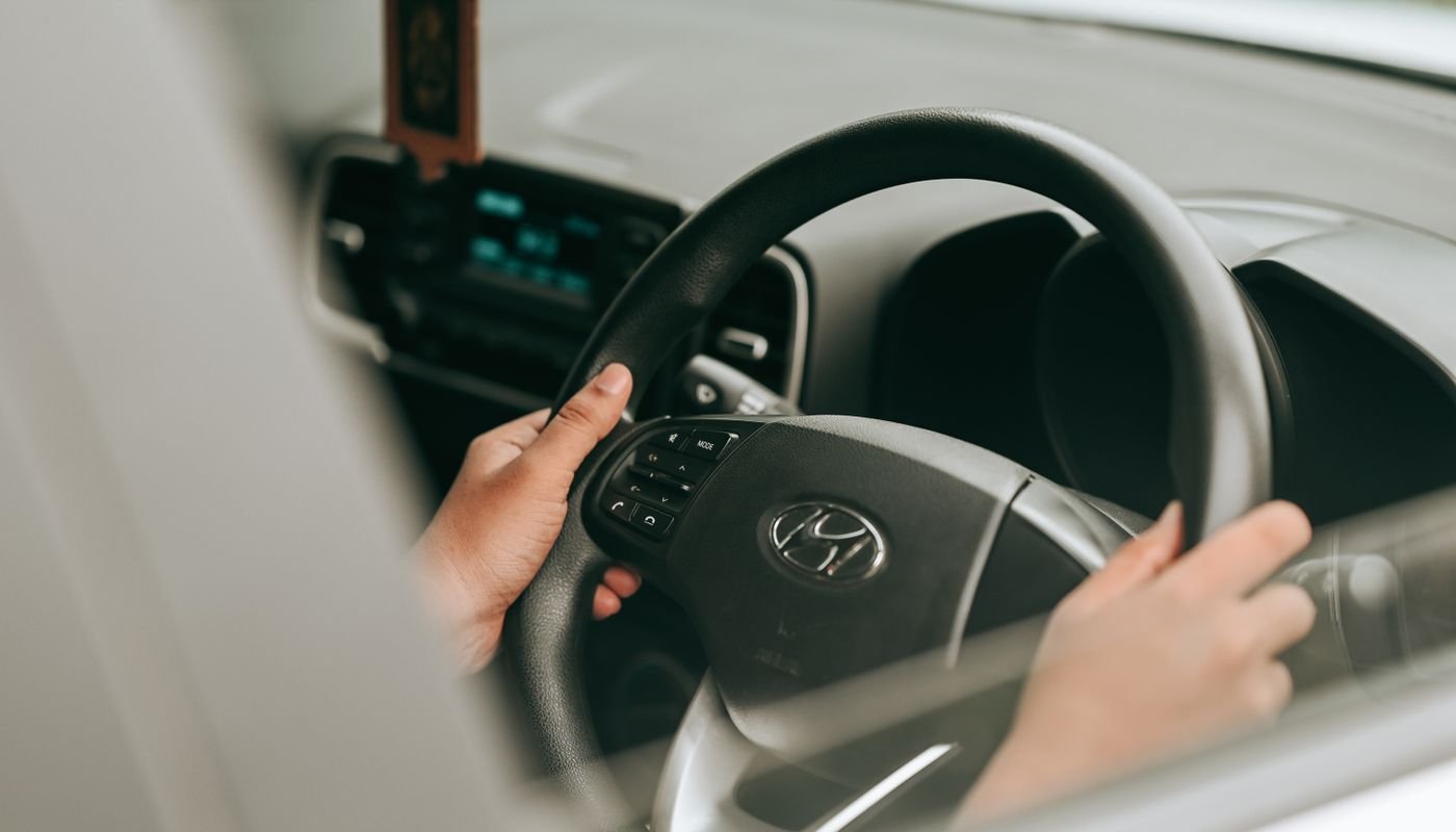 Mãos de motorista no volante de um carro, vistas pela janela do veículo