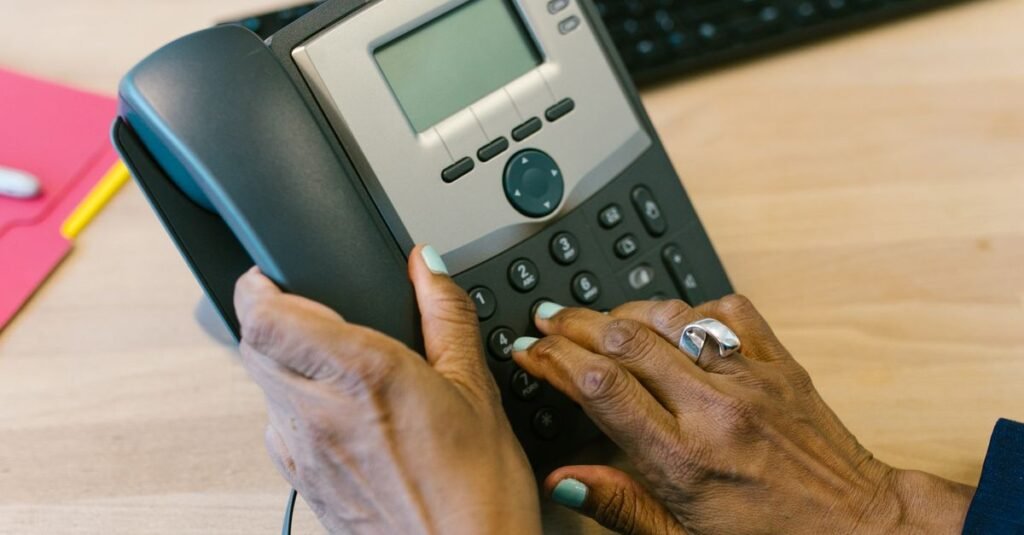 Mãos de uma mulher discando em um telefone fixo sobre uma mesa de escritório