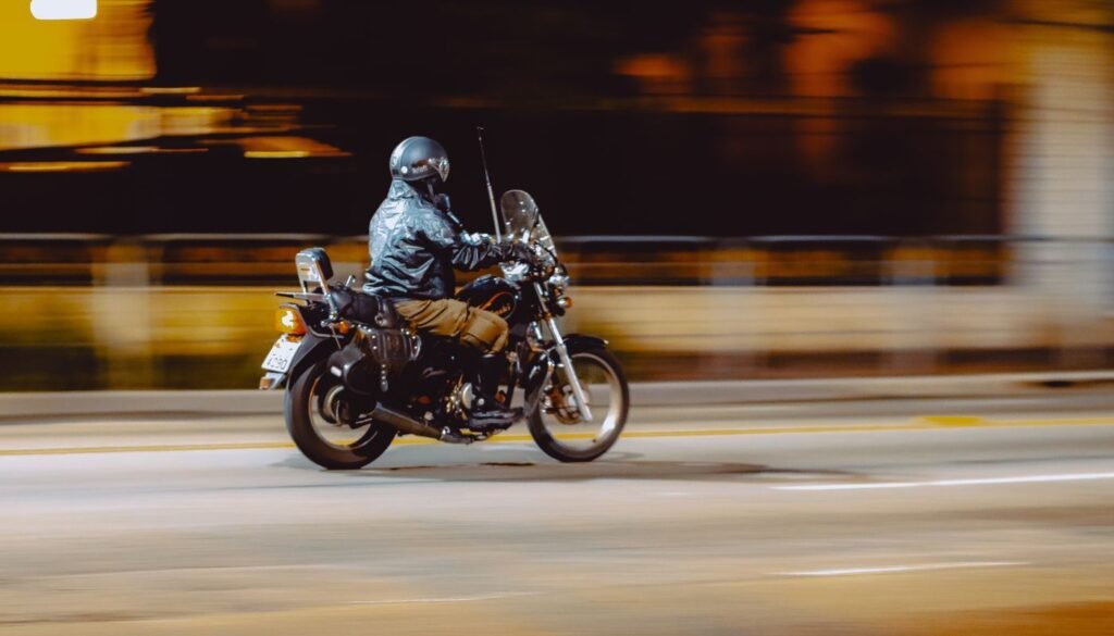 Motociclista de capacete trafega por via urbana à noite, em imagem com movimento