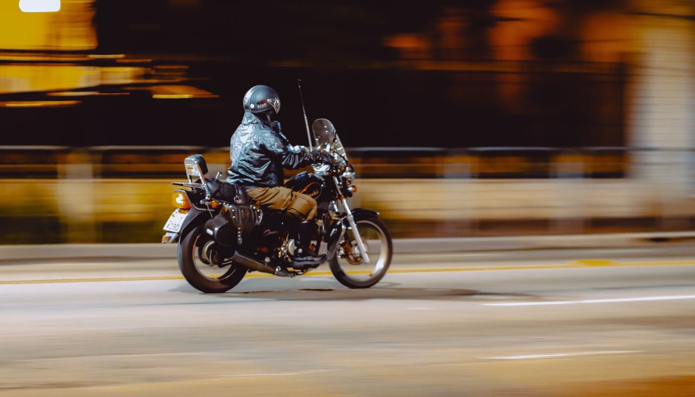 Motociclista de capacete trafega por via urbana à noite, em imagem com movimento