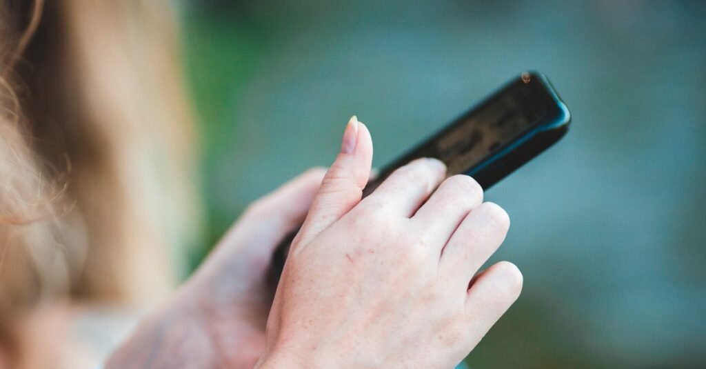 Mãos segurando um celular com a tela desligada, em close, com fundo desfocado