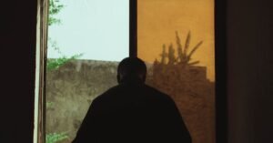 Silhueta de uma pessoa jovem diante de uma janela em ambiente com pouca luz