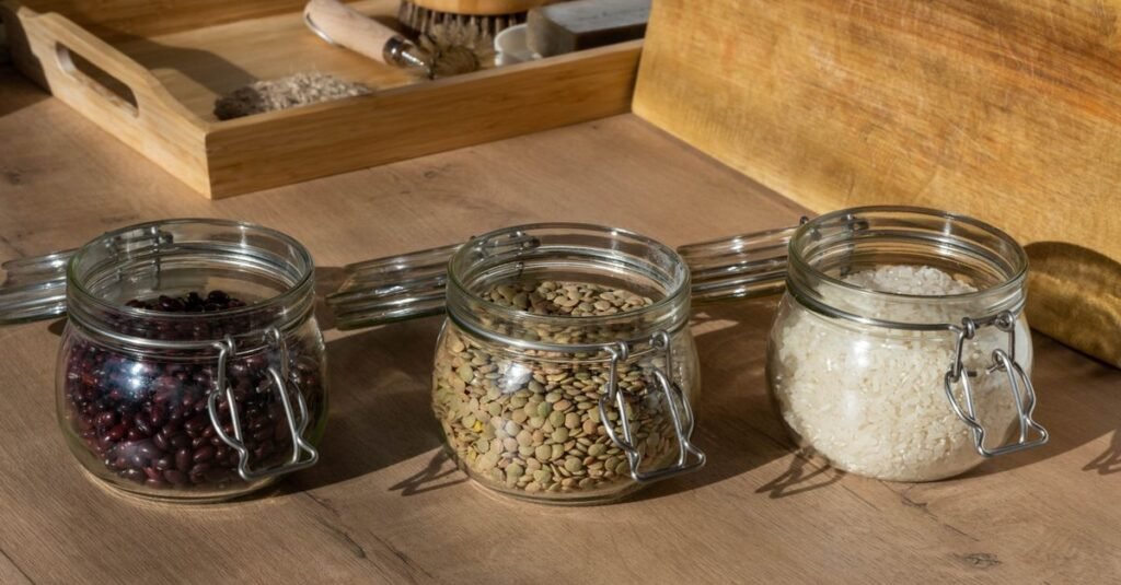 Potes de vidro com feijao, lentilha e arroz sobre mesa de madeira