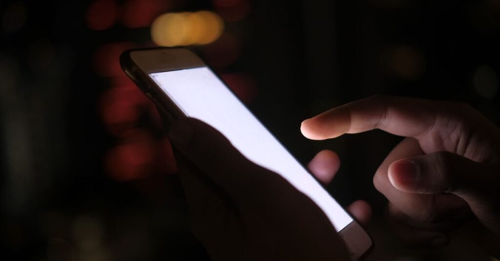 Mão usando smartphone com tela acesa em ambiente escuro