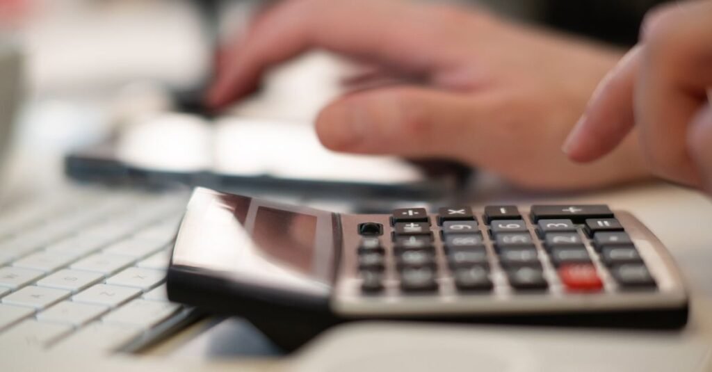 Mãos usando calculadora ao lado de um teclado de computador em mesa de escritório