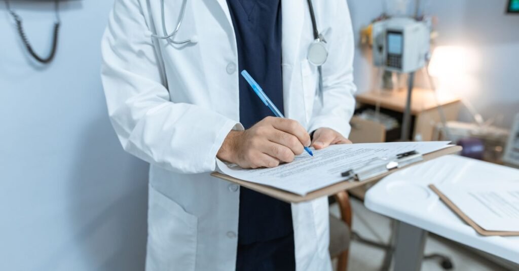Médico de jaleco branco escreve em prancheta em consultório
